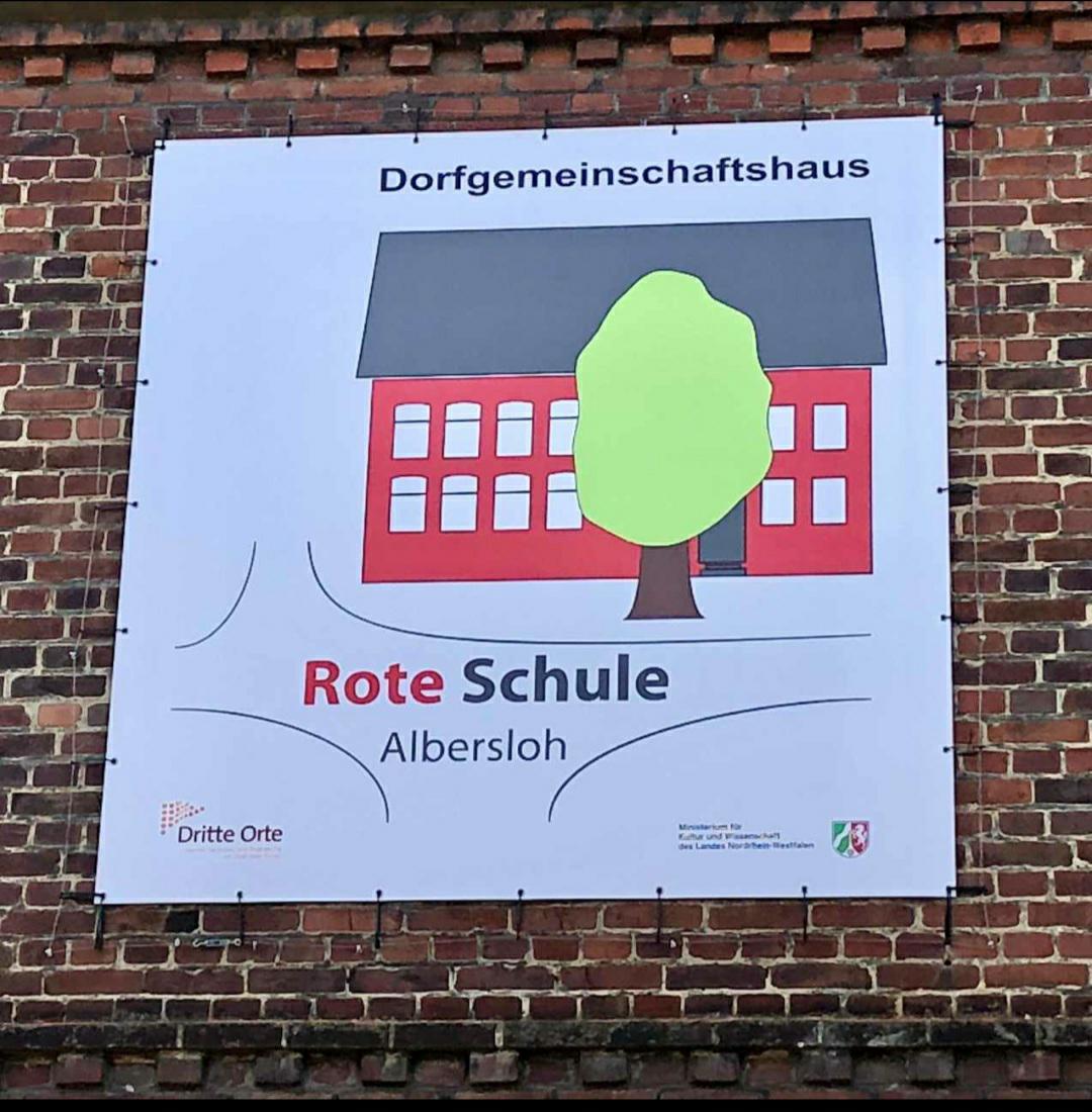 Großes Wandplakat an der Fassade der Roten Schule. Darauf ist das Logo zu sehen: rotes Haus mit grünen Baum davor und in dem Text